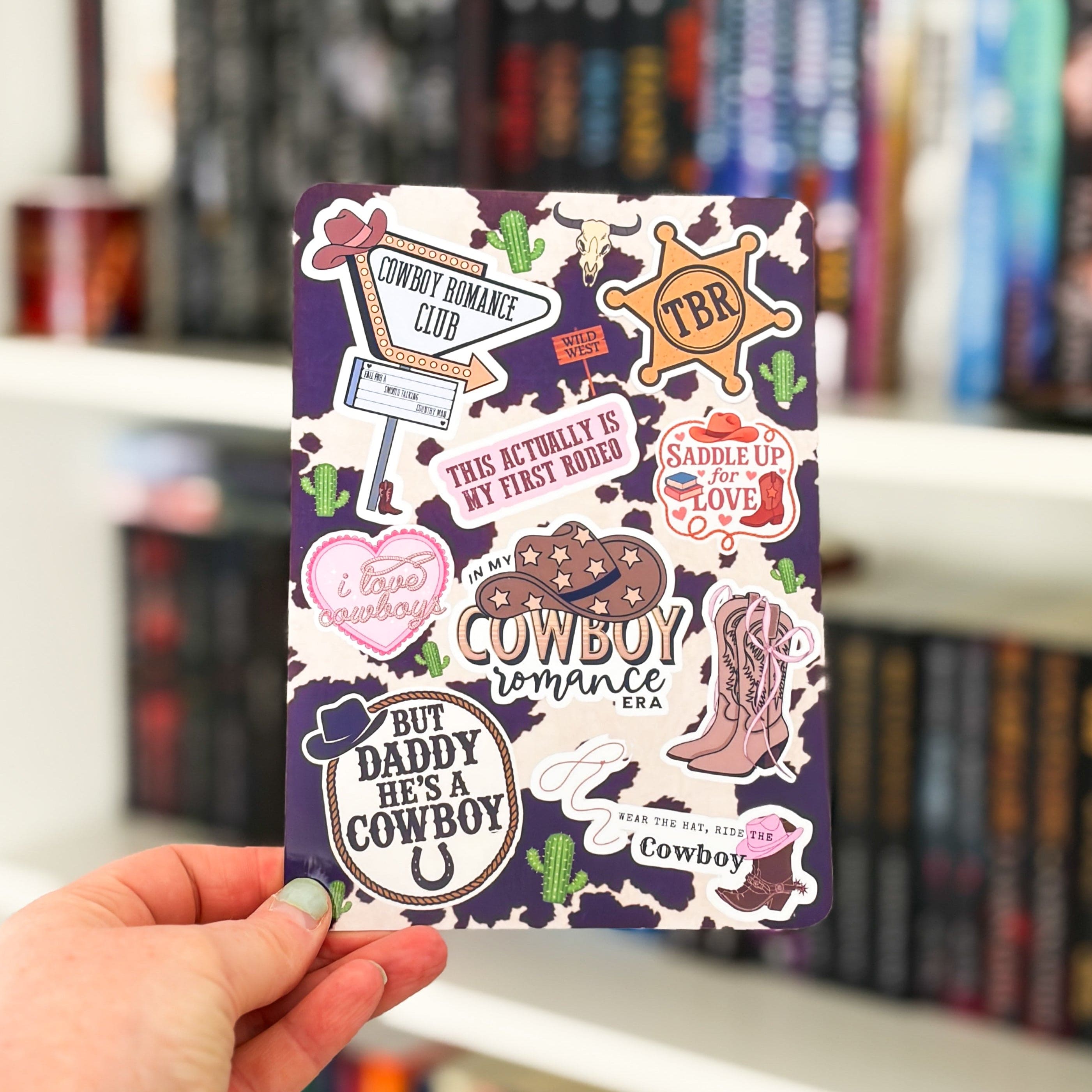 Hand holding a book with cowboy-themed stickers against a blurred bookshelf background
